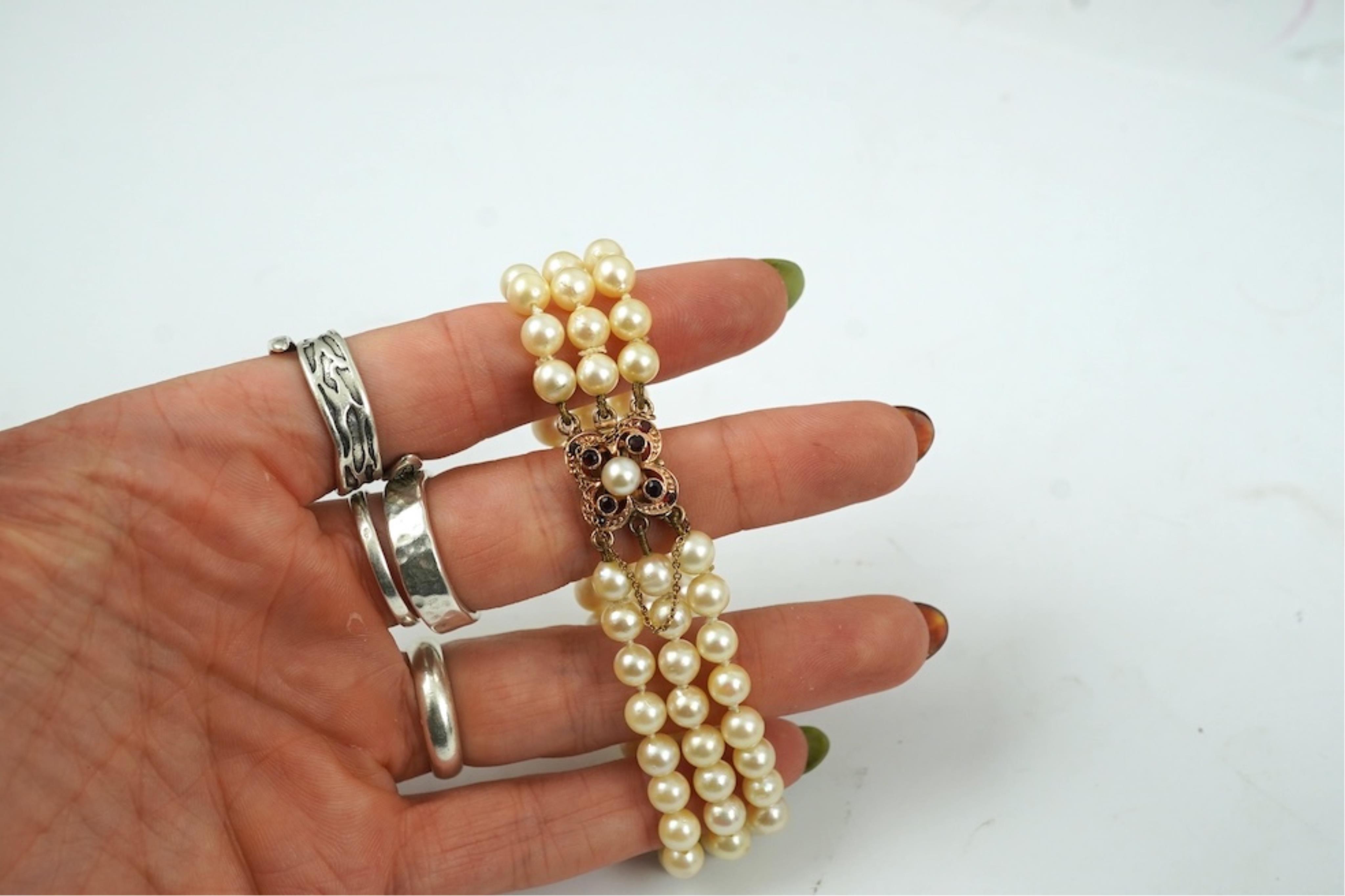 A triple strand cultured pearl bracelet, with a 9ct gold, garnet and cultured pearl cluster set clasp, 16cm.